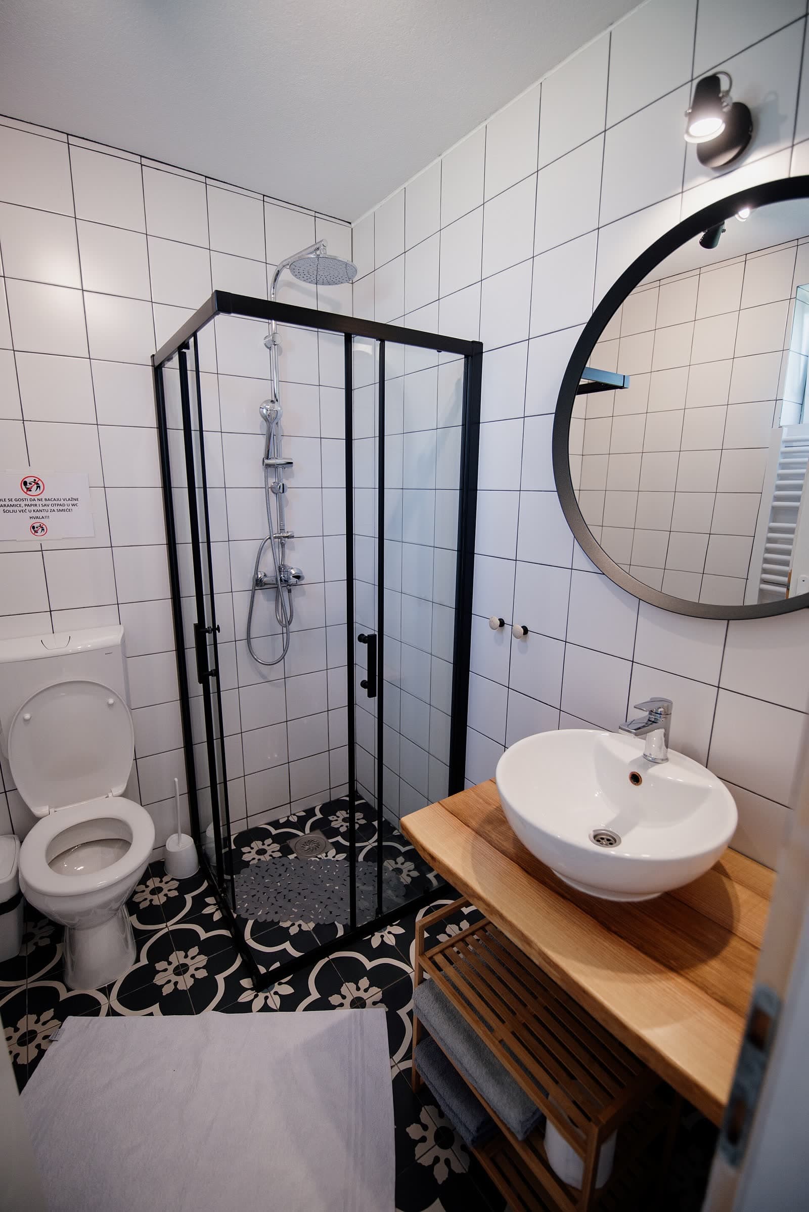 Petite salle de bain rénovée avec douche vitrée, vasque sur meuble en bois et miroir rond.