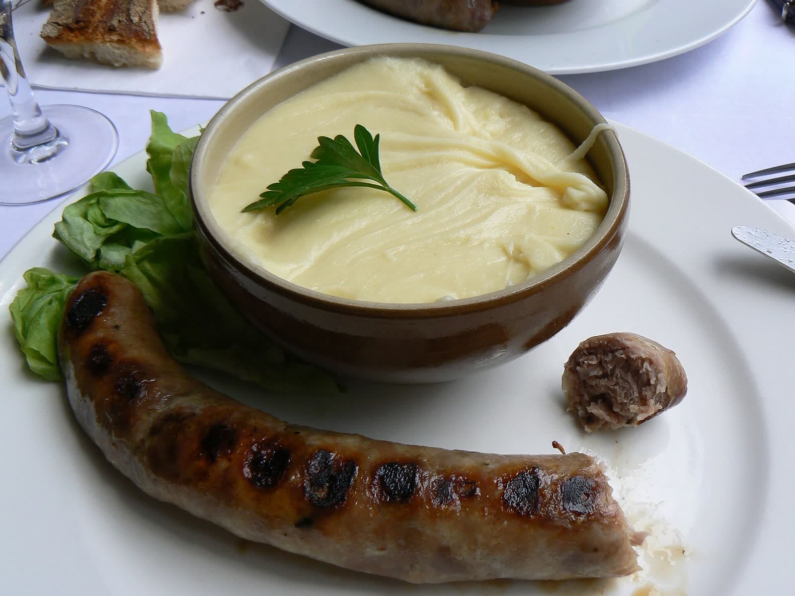 Bol d'aligot filant servi avec une saucisse grillée.
